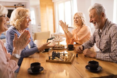 Happy seniors communicating while playing chees at home.